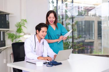 Asyalı doktor ve hemşire hasta verileri için dizüstü bilgisayar kullanarak modern klinikte birlikte çalışıyorlar. Sağlık ekibi kaliteli sağlık hizmetlerini işbirliği ve teknolojiyle sağlıyor.