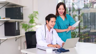 Genç Asyalı doktor ve hemşire bir dizüstü bilgisayarda iş birliği yapıyorlar ve hastane ofisinde hasta bakımını tartışıyorlar. Bu görüntü sağlık ekibi çalışmasının, tıbbi profesyonelliğin ve hasta tedavisinin özünü yakalar.