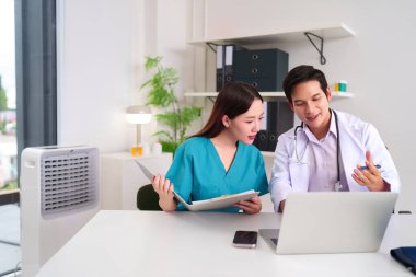 Asyalı yetişkin doktor ve hemşire klinikteki bir dizüstü bilgisayarla tıbbi kayıtları inceliyor, bir sağlık ekibi toplantısında hasta verileri ve tedavi planına danışmanlık yapıyor. Tıbbi çözüm için tartışmalar.
