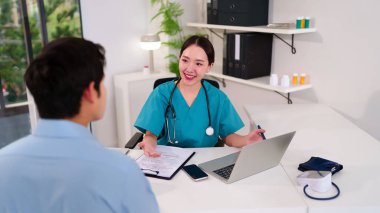 Gülümseyen yetişkin bir Asyalı kadın doktor klinikteki bir hastaya tıbbi tavsiye için danışmanlık yapıyor. Tedavi, teşhis, dizüstü bilgisayar ve teçhizat kullanılarak sağlıkla ilgili profesyonel toplantı