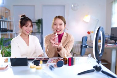 İki genç Asyalı kadın canlı yayında güzellik ürünleri ve makyaj ürünleri üzerinde inceleme yapıyorlar. Online izleyicilerle güzellik dersleri paylaşıyorlar..