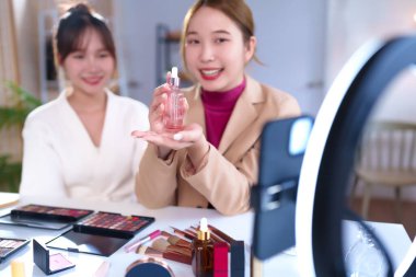 İki genç Asyalı kadın canlı bir güzellik dersi sırasında cilt serumu ürünleri sergiliyor, makyaj uygulaması ipuçlarını paylaşıyor ve evde halka ışığıyla kozmetik markasını tanıtıyorlar..