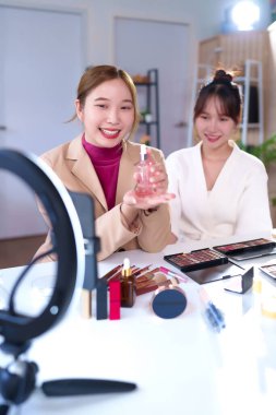 İki yetişkin Asyalı kadın online makyaj dersi yayınlıyorlar. Biri tebessümle cilt bakımı ürünü sunuyor. Güzellik ürünleri masada. Parlak ışıklandırma vlog 'u sunmaya yardımcı olur