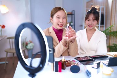 İki genç Asyalı kadın sosyal medya kanalları için güzellik içeriği yaratarak takipçilerine çevrimiçi pazarlama ve halka ışığı kullanarak yeni ürün ve makyaj paletini nasıl kullanacaklarını gösteriyorlar..