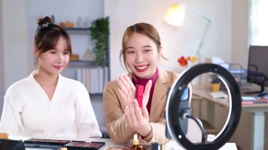 İki yetişkin Asyalı kadın online güzellik dersleri hazırlıyorlar. Parlak bir stüdyo alanında kozmetik ürünler sergiliyorlar. Sosyal medya için içerik kaydediyorlar. Makyaj için güzellik tavsiyeleri veriyorlar..