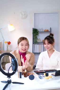 İki Asyalı kadın güzellik blogcusu, stüdyolarında sosyal medya pazarlaması için canlı yayın sırasında kırmızı ruju değerlendiriyor ve kozmetik satış ipuçları ve tavsiyelerini paylaşıyorlar.