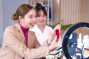 Yetişkin Asyalı kadın güzellik blogcusu canlı yayın makyajında ruj ürünü paylaşıyor. Yüzük ışığı kozmetik ürünleri değerlendirmesi yapan güzellik uzmanı için canlı yayın yapıyor.