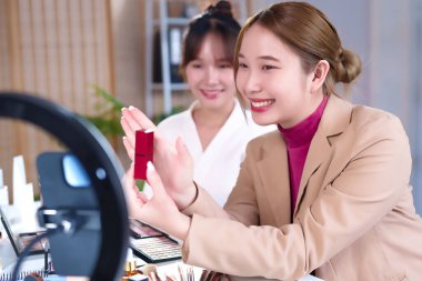 İki genç Asyalı kadın güzellik dersi kaydediyor, biri ruj tutuyor. Yüzük ışığı ve makyaj paleti, kozmetik veya güzellik markasını İnternet 'te tanıtmak için ideal bir sahne.