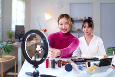 İki genç Asyalı kadın yüzük ışığı kullanarak makyaj dersi kaydediyor. Vlog incelemesi için güzellik kozmetik ürünlerini göster. Güzellik trendleri ve etkenleri hakkında çevrimiçi izleyiciler yakalamak