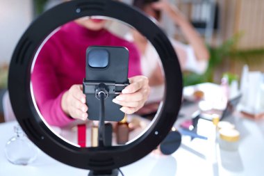 Asyalı genç kadın, evdeki güzellik dersi için yüzük ışığıyla donatılmış telefon düzeneğini tutuyor. Çevrimiçi vloglama ve cilt makyajı ve kozmetik etkiler için canlı yayın.