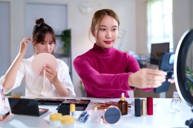 İki genç Asyalı kadın sosyal medya için güzellik ve kozmetik içeriği yaratıyor. Makyaj dersi için canlı yayında video kaydediyorlar ve ev stüdyolarında ürün değerlendirmesi yapıyorlar..