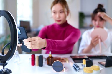 Asyalı genç kadınlar video oluşturma için kozmetik ürünleri uygulayarak ve sunarak vlog için halka ışıkları ile güzellik dersleri oluşturuyorlar ve makyaj yapıyorlar.