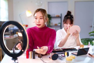 Genç Asyalı kadınlar makyaj ürünleri halka ışığı kullanarak çevrimiçi platformlar için güzellik içeriği oluşturuyorlar. İçerik yaratıcısı sosyal medya güzellik videoları için makyaj dersleri sağlıyor.