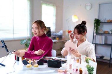 İki genç Asyalı kadın çeşitli kozmetik ürünleriyle birlikte makyaj dersini canlı olarak yayınlıyorlar. Bu, sosyal medya ve pazarlama kampanyaları için mükemmel bir fırsat.