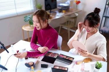 İki genç Asyalı kadın çeşitli kozmetik ve güzellik ürünleri içeren bir makyaj dersi hazırlıyorlar. Güzellik tavsiyelerini ve sosyal medyada cilt bakımı ve cazibe tekniklerini paylaşıyorlar.