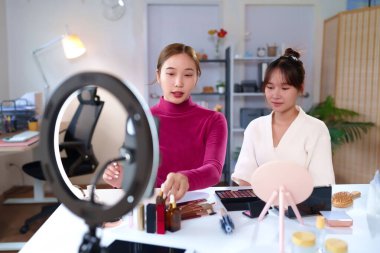 Sosyal medya için canlı yayında farklı güzellik ürünleri ve kozmetik ürünleri sunan ve tanıtan iki Asyalı genç kadın..