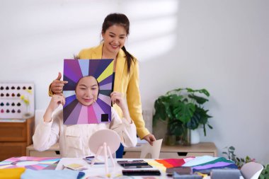 İki Asyalı kadın kişisel renk analizi yapıyor. Genç bir kadın için en iyi makyaj ve giysi renklerini belirlemek için renk paleti kullanıyorlar..