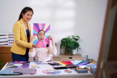 İki genç Asyalı kadın, güzellik salonunda ten rengine uyan en iyi makyaj kıyafetlerini ve saç renklerini bulmak için kişisel renk analizi yapıyorlar.
