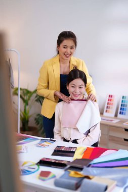 İki Asyalı kadın, kumaş örnekleri seçerek gülümsüyor ve moda tasarım stüdyolarında ahenk bulmak için kişisel renk danışmanlıklarını değerlendiriyorlar..