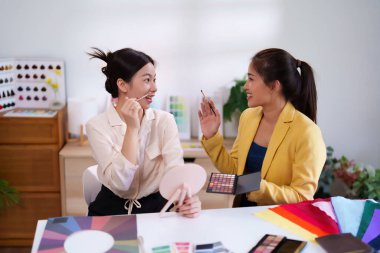 Asyalı kadınlar renk seçerek kişisel renk analizi yapıyorlar. Makyaj sanatçısı, genç müşterisinin fırçalı mükemmel paleti bulmasına yardım eder..