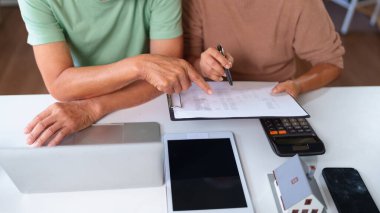 Yaşlı çift evlerinde mali belgeleri inceliyor. Birlikte emeklilik tasarrufu ve ev yatırımları yapmayı planlıyorlar. Teknolojiyi yardım etmek için kullanıyorlar..