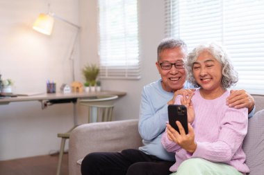 Mutlu son sınıf Asyalı çift evdeki cep telefonundan ailelerini ararken videodan zevk alıyor. Emeklilik hayatını ve aile bağlarını benimse.!