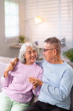 Bu iç açıcı görüntü, yaşlı bir Asyalı çiftin evde sevgi dolu bir anı el ele tutuşup gülümsemesini gösteriyor. Emeklilik mutluluğu ve aşkı göstermek için mükemmel..