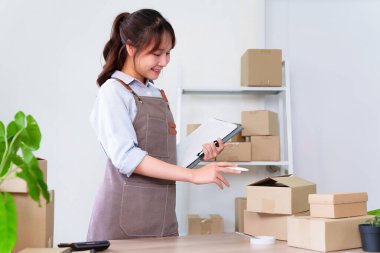 Bu genç Asyalı bir kadının karton kutular hazırlayan panodaki ürün stoklarını kontrol edişinin bir resmi. E-ticaret işi için teslimat servisine hazırlanıyor..