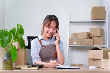 Asyalı bir girişimci kadın emir alıyor ve küçük işletmelerini evden yönetiyor. İnternetteki işi için sipariş detaylarını yazarken telefonda konuşuyor..