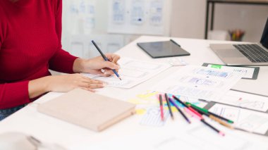 Asyalı yetişkin bir kadın kağıt üzerinde web tasarımı yapıyor. Kullanıcı arayüzü tasarımcısı işte, el çizimi kablo çizimi ile mobil uygulama geliştiriyor.