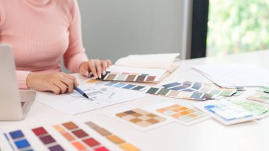 Genç Asyalı kadın iç mimar, masadaki dizüstü bilgisayarla web sitesi veya uygulama projesi için renk seçimi üzerinde çalışıyor. Kullanıcı deneyimi tasarım işi planlanıyor.