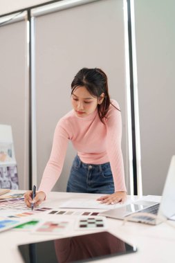 UI UX tasarımcısı olarak çalışan Asyalı yetişkin bir kadın mobil uygulamalar ve web siteleri gibi dijital ürünler için bir renk paleti kullanarak arayüz düzeni yaratıyor.