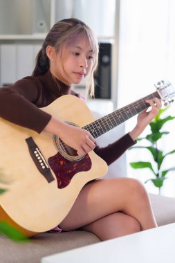 Genç bir Asyalı kadın evinde akustik gitarını mutlulukla çalıyor. Müziği seviyor. O, bir şarkıyla rahatlatıcı hobisinin tadını çıkarıyor..