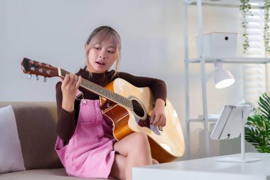 Asyalı bir kadının akustik bir gitarla müzik çalarken, rahat koltuğunda dinlenirken, Asyalı bir sanatçının evinde müzik tutkusu dolu bir hayat tarzının büyüleyici bir görüntüsü..