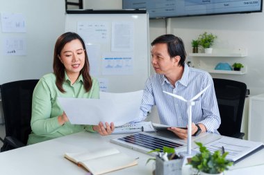 Asyalı iş adamları sürdürülebilir enerji çözümleri ve ESG girişimlerini çağdaş bir ofiste inceliyorlar. Yenilenebilir teknoloji modelleriyle planları gözden geçiriyorlar..