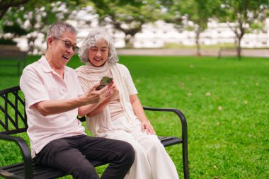 Güneşli bir parkta bankta oturan yaşlı bir Asyalı karı koca bir cep telefonuna bakarak keyifli bir anı paylaşıyor.