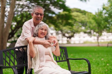 Yaşlı Asyalı çift, sevgi dolu emeklilik anını paylaşıyor. Sevgi dolu park bankında sevgi simgesi oluşturan eller açık havada keyif çatıyor.