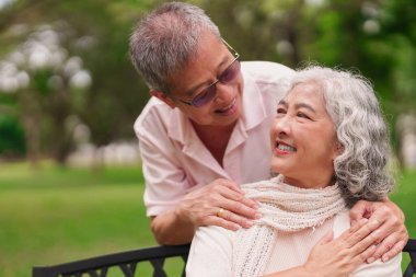 Kıdemli Asyalı adam, altın yıllarında huzurlu bir park ortamında karısına sevgi ve neşe göstererek doğanın tadını çıkarıyor.