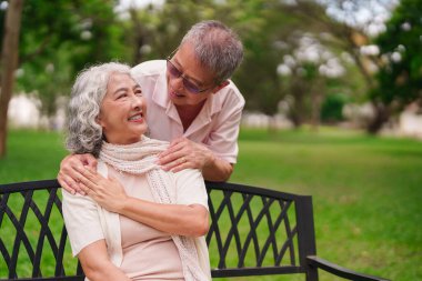 Mutlu son sınıf Asyalı çift açık hava parkının tadını çıkarsın. Emekli koca, sevgi ve neşe içinde karısını kucaklıyor..