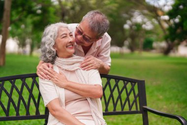 Asyalı yaşlı bir adam ve kadın parkta bir bankta oturup birbirlerine bakıyorlar ve birbirlerine sevgi dolu bir şekilde emeklilik hayatlarının tadını çıkarıyorlar.