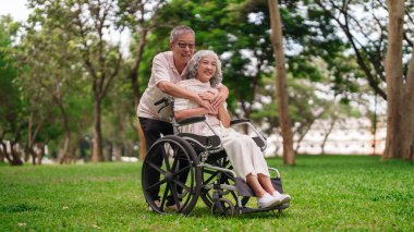 Kıdemli Asyalı koca güzel bir parkta karısını kucaklıyor. Mutluluk ve karşılıklı destek paylaşıyor. Altın yılı kutluyor.