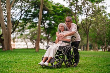 Asyalı yaşlı adam dışarıda tekerlekli sandalyedeki kadını destekliyor. Doğanın ve arkadaşlığın tadını çıkarırken mutlu görünüyorlar. Emeklilik hayatı zarif bir şekilde yaşlanıyor.