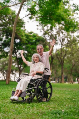 Asyalı yaşlı çift parkta eğleniyor tekerlekli sandalyedeki kadın arkalarında duruyor ve aktif emekliliklerini kutluyorlar.