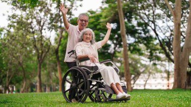 Mutlu Asyalı yaşlı çift parkta eğleniyor. Tekerlekli sandalyedeki kadını iten adam sağlıklı yaşam tarzını kutluyor.