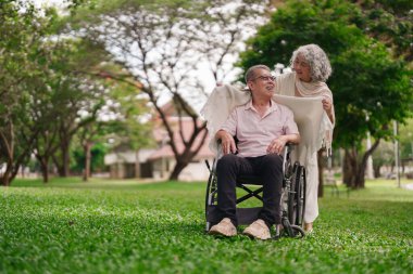 Yaşlı Asyalı çift parkın tadını çıkarıyor. Temiz hava alıyor. Tekerlekli sandalyede kocasına bakıyor.