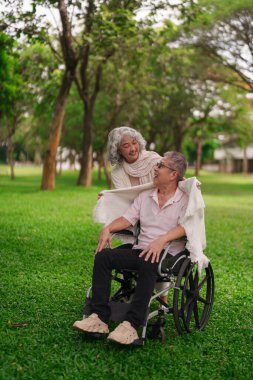 Yaşlı Asyalı çift, yeşil parkta birlikte sevgi dolu anlar yaşıyor. Emeklilik süresince sevgi ve destek gösteriyorlar.