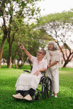 Mutlu Asyalı yaşlı çift dışarıda eşleriyle vakit geçiriyorlar. Tekerlekli sandalyede kocalarıyla ilgileniyorlar. Birlikte eğleniyorlar.