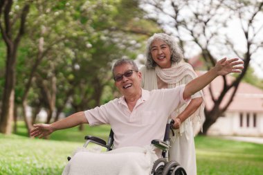 Parktaki mutlu Asyalı yaşlı çift tekerlekli sandalyedeki kadınla birlikte dışarıda emeklilik sonrası özgürlüğün tadını çıkarıyorlar.