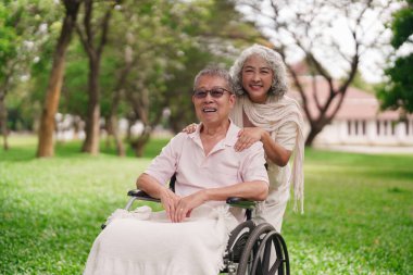 Asyalı yaşlı çifti seven açık hava parkı karısı, tekerlekli sandalyede kocasını destekliyor ve birlikte doğanın tadını çıkarıyorlar..