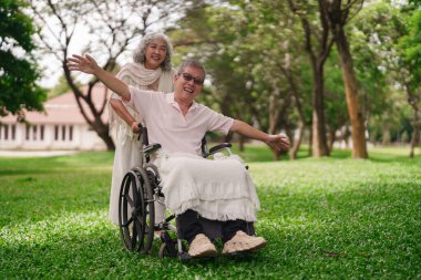 Asyalı yaşlı çift, emeklilikten sonra birlikte mutlu mesut vakit geçiriyorlar tekerlekli sandalye kullanımına destek ve bakım sağlıyorlar.